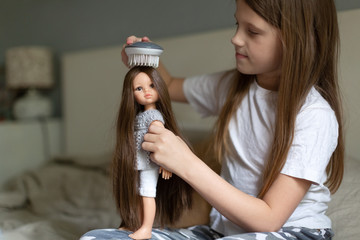Caucasian girl combing a doll with long hair, a girl playing dolls. Traditional children's games...