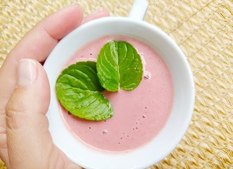 Woman's hand holding cup of strawberry smoothie with mint leaves