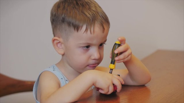Shooting a portrait of a cute preschool boy, the child repairs his favorite red toy car for kids with a screwdriver, screws a screw, performs a real working sitting at a table at home.