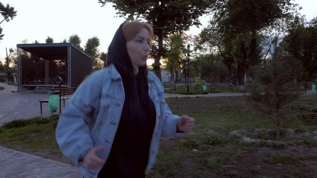 girl in a hood and a denim jacket jogs in the city park