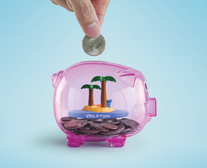 Money savings for vacation or traveling concept. Hand putting a coin into a pink piggy bank with an...
