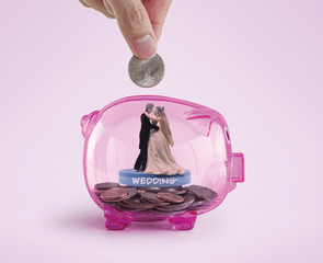 Money savings for wedding or marriage concept. Hand putting a coin into a pink piggy bank with...