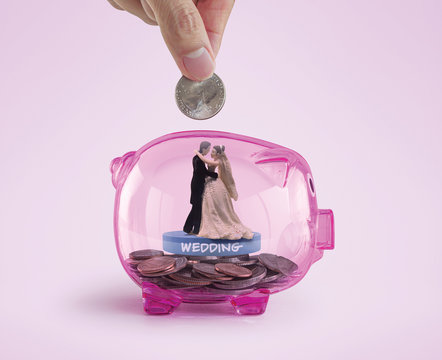 Money savings for wedding or marriage concept. Hand putting a coin into a pink piggy bank with bride and groom toy inside.