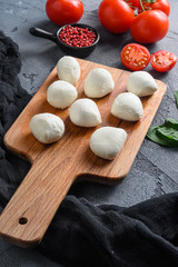 Buffalo Mozzarella cheese balls with fresh basil leaves and cherry tomatoes, the ingredients of the Italian Caprese salad, on a black cloth and grey concrete background close up vertical