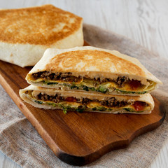 Tasty Homemade Beef Crunchwrap Quesadilla on a rustic wooden board on a white wooden table, low angle view. Close-up.