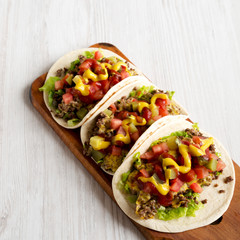 Homemade Cheeseburger Tacos on a rustic wooden board on a white wooden surface, low angle view.