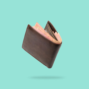 Flying in air Brown genuine leather wallet with banknotes and credit card inside isolated on turquoise background.