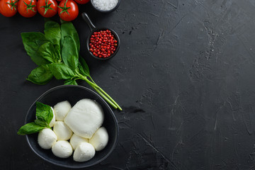 Mini balls of mozzarella cheese,Fresh cherry tomatoes, basil leaf, cheese for caprese salad on black slate stone chalkboard with copyspace.  Top view
