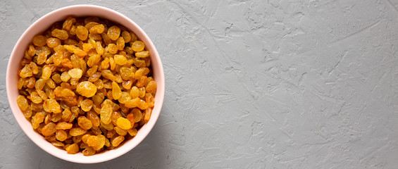 Golden Raisins in a Pink Bowl on a gray background, top view. Flat lay, overhead, from above. Copy space.