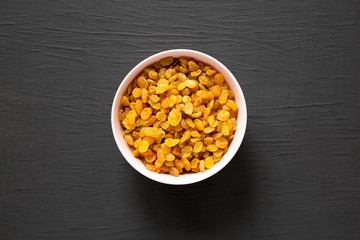 Golden Raisins in a Pink Bowl on a black surface, top view. Flat lay, overhead, from above.