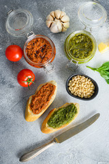 Fototapeta na wymiar Glass jars with red and green pesto Parmesan cheese, basil leaves, pine nuts, olive oil, garlic, salt, tomatoes breakfast panini with sauce top view on grey concrete surface