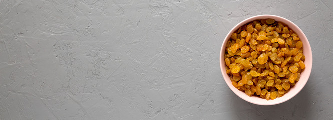 Golden Raisins in a Pink Bowl on a gray surface, top view. Flat lay, overhead, from above. Copy space.