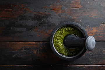 fresh Green basil pesto  preparation in black mortar over old wood table copy space for text overhead