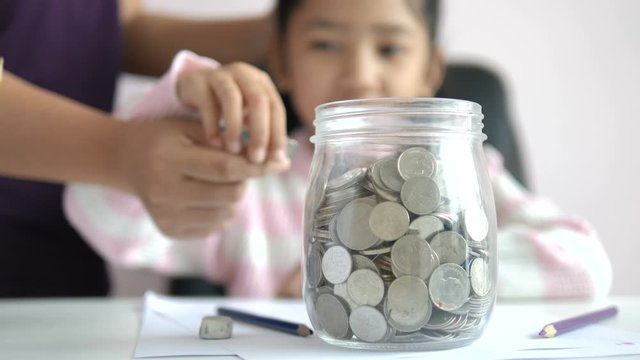Asian little girl putting the coin in to a glass jar shallow depth of field select focus on jar