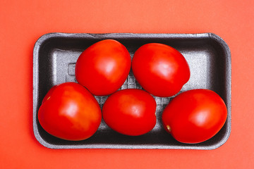 Tomatoes in a black plastic container on a red background. Top view. Shiny vegetables.
