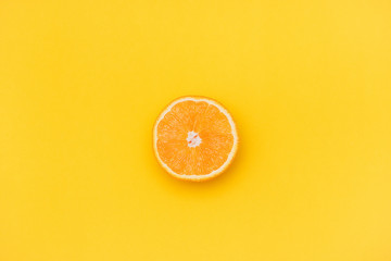 One half of an orange on a yellow background. Orange is in the middle of the picture. Copy space.