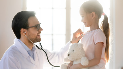 Caring male doctor listen to little girl patient heartbeat with stethoscope at regular hospital checkup, man GP or pediatrician examine small child client health at consultation, healthcare concept