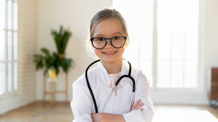 Happy cute little preschooler girl in white medical uniform and glasses act like doctor, portrait...
