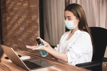 Young woman working from home wearing protective mask. .Business woman in quarantine for coronavirus. Working from home. Cleaning her hands with sanitizer gel.