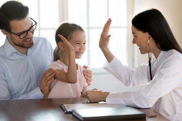 Happy young father and small little daughter greeting give high five to female pediatrician at meeting in clinic, smiling woman doctor GP consult small girl child patient in hospital, healthcare