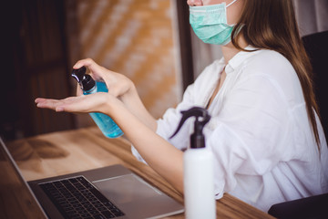 Business woman working from home wearing protective mask..in quarantine for coronavirus. Cleaning her hands with sanitizer gel for protect pandemic health risk