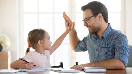 Overjoyed dad and little preschooler daughter give high five celebrate success in studying, smiling...