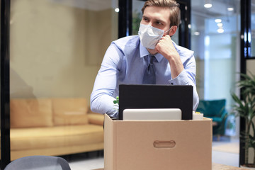 Dismissal employee in preventive medical mask in an epidemic coronavirus. Sad dismissed worker are taking his office supplies with him from office.