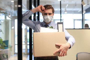 Dismissal employee in preventive medical mask in an epidemic coronavirus. Dismissed worker going from the office with his office supplies.