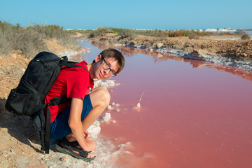 Handsome young happy boy at extremely salty pink lake, colored by microalgae with crystalline salt depositions in Torrevieja, Spain, Europe. Teen boy  walking at lake with crystals of salt. 