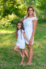 Fototapeta premium Little girl hugs mother, summer nature outdoor. Mom and daughter wearing white clothes against summer greenery. Family walks in park. Trust, kindness, maternity, parenthood, confidence, mother's love