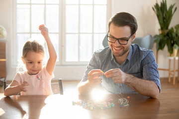Overjoyed young dad and little preschooler daughter thread wooden bead making bracelets at home...