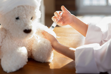 Close up of small girl in medical uniform act as doctor give injection to plush teddy bear, little child in whites play in hospital vaccinate prick fluffy toy, engaged in game, future career concept - obrazy, fototapety, plakaty