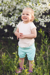 Cute baby girl on a background of white blossoms of an apple tree