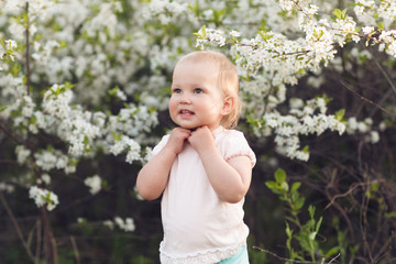 Cute baby girl on a background of white blossoms of an apple tree