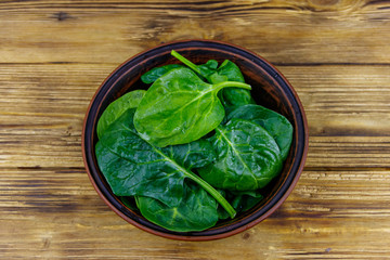 Fresh green spinach leaves in bowl on a wooden table. Top view