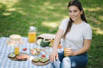 Woman hold disposable cup with orange lemonade on picnic outdoors. Space for text. Vegan picnic concept