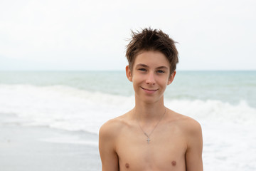 Fototapeta na wymiar Handsome young boy at beach, summer vacation. Portrait of beautiful calm smiling teen boy at sea coast posing after swimming. Travel, summer vacation, tourism, teenage lifestyle, recreation