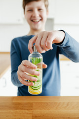Teenager boy holding glass bottle infused detox water with cucumber, lemon and mint