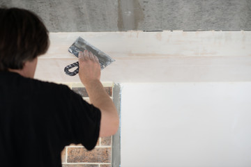 Putty knife in male hand. Hand workю Worker putsty plasterboard ceiling in new appartment. Repairman works with plasterboard, plastering dry-stone wall, home improvement. Man makes repairs at house.