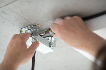 Man fastens a mortgage for the lamp to the ceiling. Men's hands with a screwdriver. DIY home repair. The master makes repairs in the new building, detail