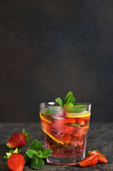 Lemonade with strawberries and mint on a dark concrete background. Summer cold drink.