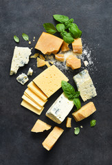 Cheese set: brie, blue cheese, parmesan and basil on a black concrete background. View from above.