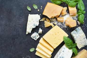 Cheese set: brie, blue cheese, parmesan and basil on a black concrete background. View from above.