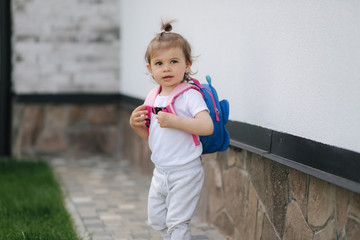 Cute little girl with backpack walk near the house
