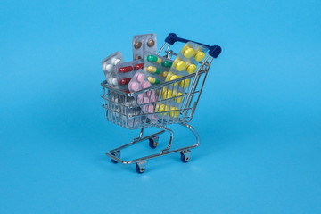 A variety of pills in a supermarket trolley on a blue background.