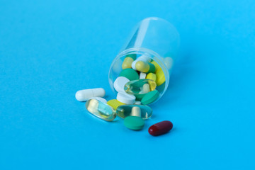 Assorted pills and capsules, a bottle on a blue background. Pharmaceutical medicine.