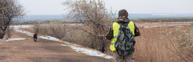 Silhouette of a hunter with a gun in the reeds against the sun, an ambush for ducks with dogs