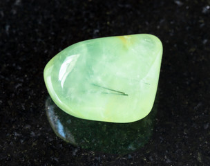 closeup of sample of natural mineral from geological collection - rolled Prehnite rock on black granite background from Republic of Mali