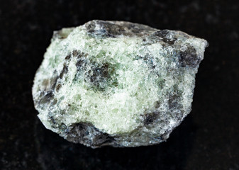 closeup of sample of natural mineral from geological collection - rough saccharoidal Apatite rock on black granite background from Khibiny, Kola Peninsula, Russia
