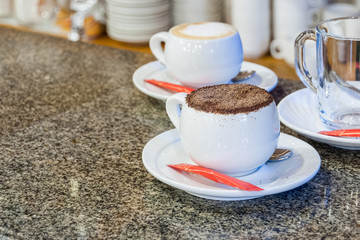Fresh cappuccino in white cup is staying on bar stand